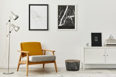 White retro living room with framed maps, designer armchair, lamp. Modern home decor.