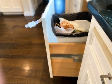 time for dad to take out family’s trash: open cabinet showing full trash can