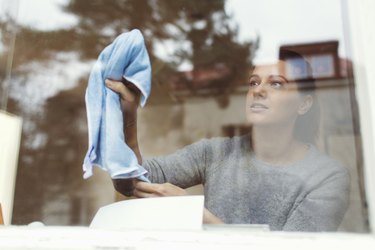 Woman cleaning inside surface of window.