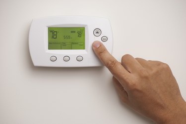 Hand on digital thermostat set at 78 degrees