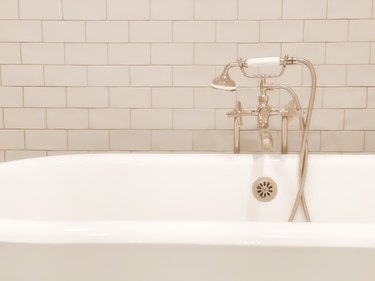 Old-fashioned polished nickel cross handle bathtub faucet & handheld sprayer with white enameled antique cast iron claw foot tub.