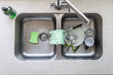 Overhead shot of a sink showing scrubbing gloves and a scouring pad. All them are green