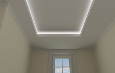 Ceiling close-up in classic interior, vintage room with stucco and moldings, beige wallpaper, illuminated false suspended ceiling design