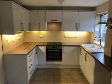 Image of empty rental property kitchen, magnolia painted walls, tiled flooring, oven, white cupboards with under lighting