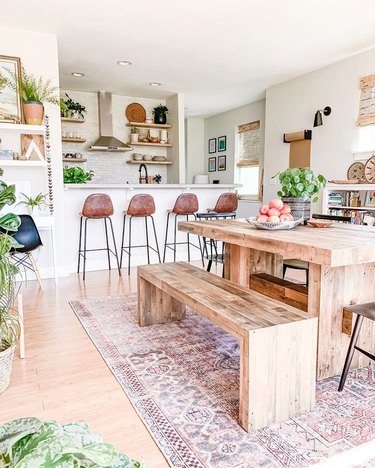 White and wood contemporary dining room with a lot of plants, natural wood dining picnic table, and minimal tan leather stools with black metal legs