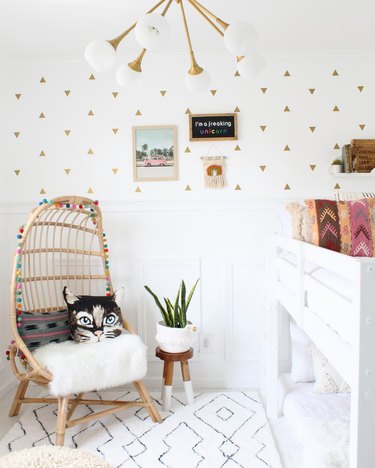 All-white child's room with gold triangle wall decals, midcentury pendant light, rattan chair, and white bunkbeds