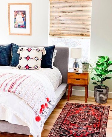 Bohemian bedroom with wooden midcentury nightstand, textured pillows, and gray headboard