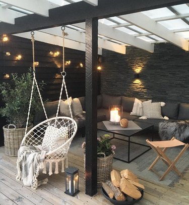 Black patio with string lights, L-shaped black couch, and hanging rope circular hammock chair