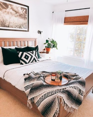 Minimal southwestern-inspired bedroom with black and white mexican blanket and dark green velvet throws on white bedding