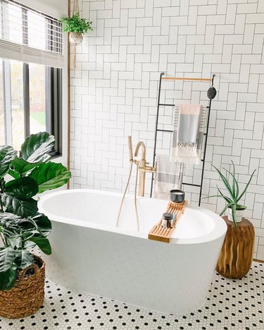 Minimal white bathroom with ladder towel rack, wooden tub caddy, and tree stump plant holder