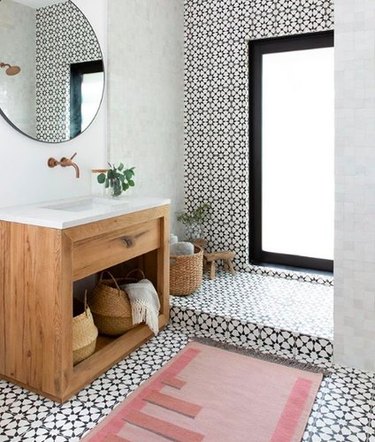 Minimal bathroom with floor-to-ceiling black and white tile, blush geometric rug, and wooden minimal vanity