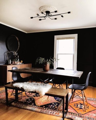 Black dining room with black midcentury dining chairs, wood and metal dining table, wood and metal bench, and black edison bulb chandelier