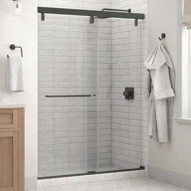A bathroom with a sliding shower door with black matte finish and a white robe hanging next to it