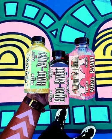 Bingo-Bango Fresh Fruit Soda Co. soda bottles in front of colorful geometric mural.
