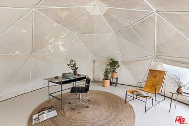 A dome-shaped room in cream with triangular panels with a desk, chair, and some plants.