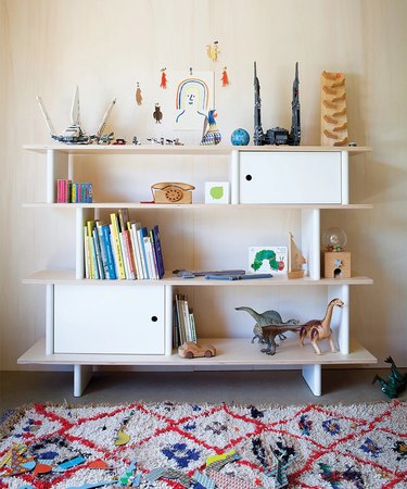 A white children's shelving unit topped with books and toys.