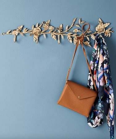 Gold flowered hook rack against a blue wall with a purse and scarf hanging from it