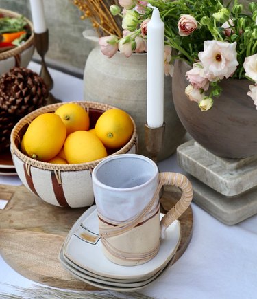 tabletop area with a bowl of fruit, a candle, and a mug on a dish