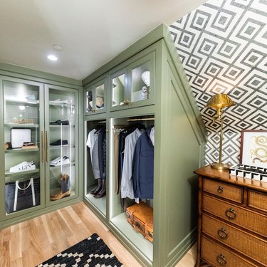 Walk-in closet with green cabinetry, geometric wallpaper and antique lookign wood dresser.