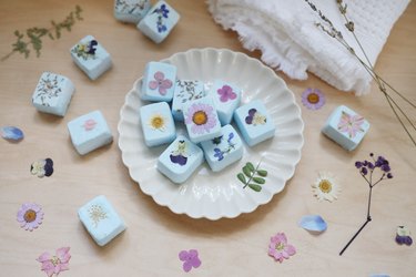 DIY Shower Steamers with pressed flowers arranged on a fluted plate next to a towel