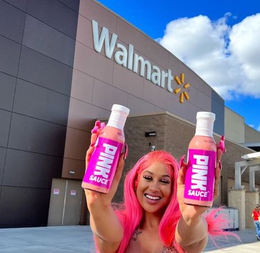 Creator Chef Pii holding up two bottles of Pink Sauce in front of a Walmart store.