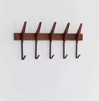 wall-mounted dark wood coat rack with long black hooks on a gray background.