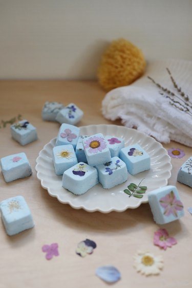 DIY Shower Steamers with pressed flowers arranged on a fluted plate next to a towel