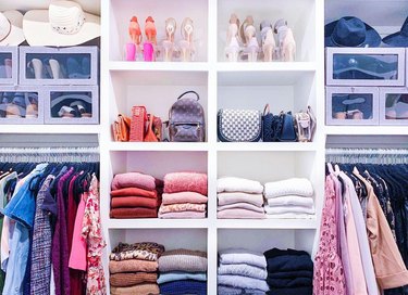Detail of a walk-in closet with white shelving and clothing arranged by color and category.
