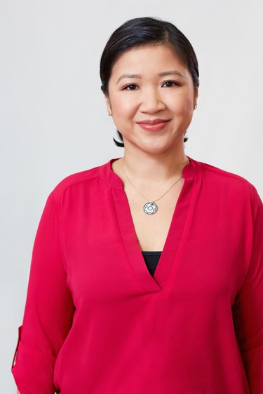 Joanne Kwong wearing a magenta, V-neck shirt and silver necklace and her black medium-length hair pulled back.