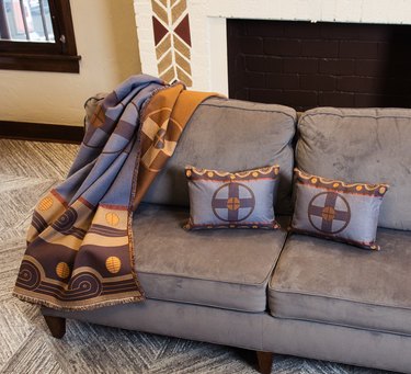 A gray couch with two Mahota Textile pillows and a matching blanket draped over the side.