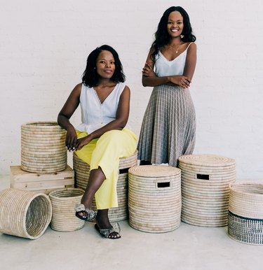 two women, one sitting and one standing, surrounded by baskets
