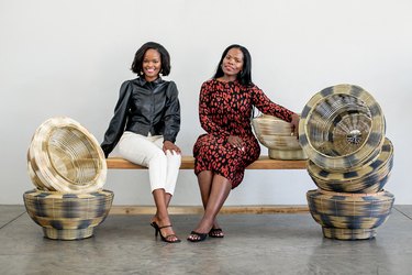 two people sitting on a bench, with a pile of baskets on either side of them