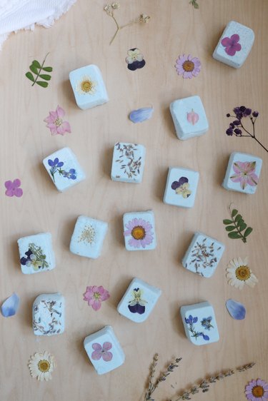 DIY Shower Steamers with pressed flowers on a wood surface next to a white towel