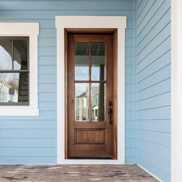 A wooden front door with large glass panes on a house with blue siding