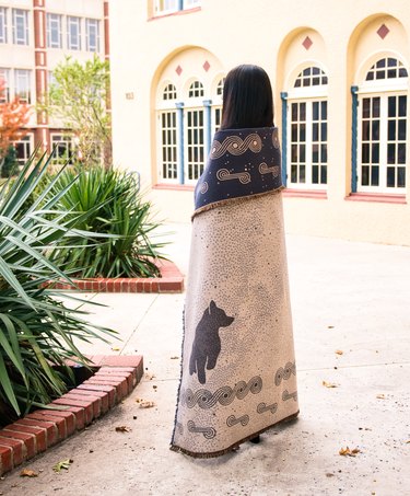 A person facing away wrapped in a Mahota Textiles blanket in a courtyard.