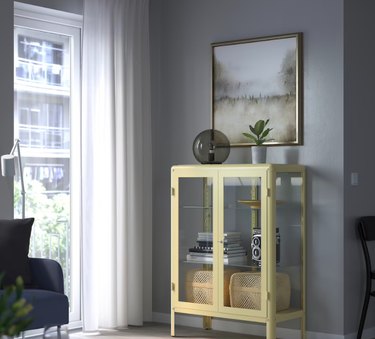 yellow IKEA fabrikör with baskets, books, and decor items near framed art and window