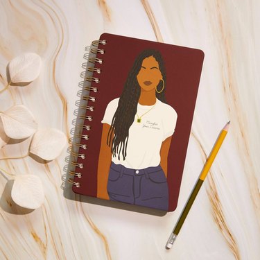 overhead photo of wood table with pencil and journal with illustration of a figure in a t-shirt and jeans