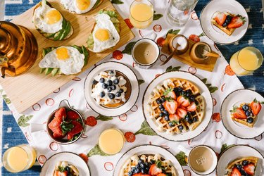 Breakfast spread from above including waffles with fruit, sunnyside up eggs, avocado toast, orange juice, and coffee.