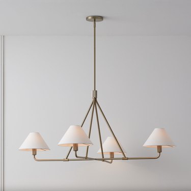 Bronze chandelier with white shades against a white wall.