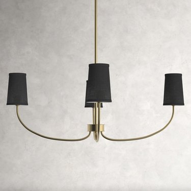 4-light gold chandelier with black lamp shades against a gray wall