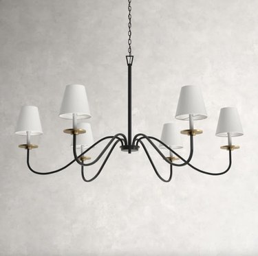 6-light black metal chandelier with white shades against an off-white wall.