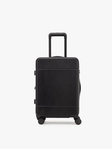 The Calpak Hue Carry-On in black with the handle slightly extending over a white background.
