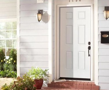 A white steel front door on a house with white siding and a brick front porch