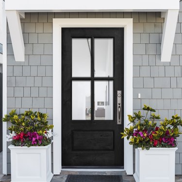 A wood front door on a home with cedar shake siding; two white planters are filled with flowers