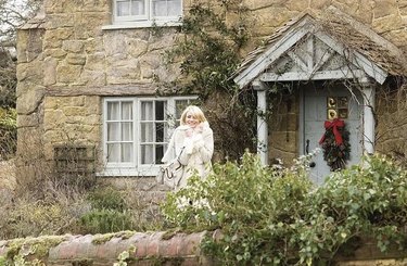Cameron Diaz wears a cream coat and carries a cream bag as she walks out of a cottage in the English country side in the movie, The Holiday.