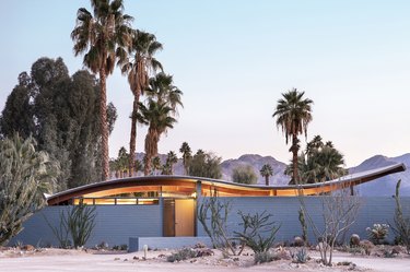 The Wave House, now called The Desert Wave, in the Coachella Valley surrounded by palm trees with mountains and a light blue sky in the background.