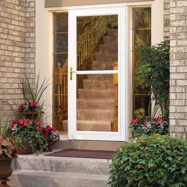 A white storm door on a brick house with lots of plants on the front porch
