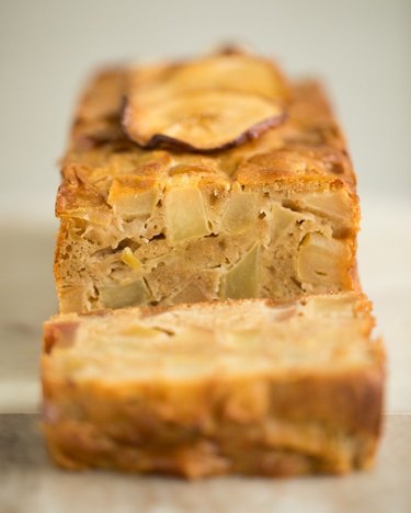 A rectangular loaf of apple tea cake with one cut slice