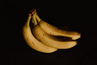 A photo of three ripe bananas with brown spots on a black background.
