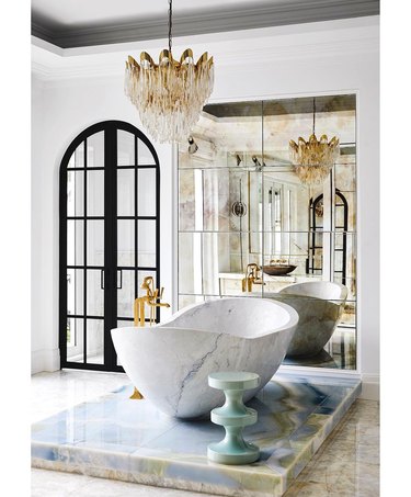 Hollywood regency contemporary bathroom with crystal and brass chandelier, marble tub and pedestal table and brass hardware